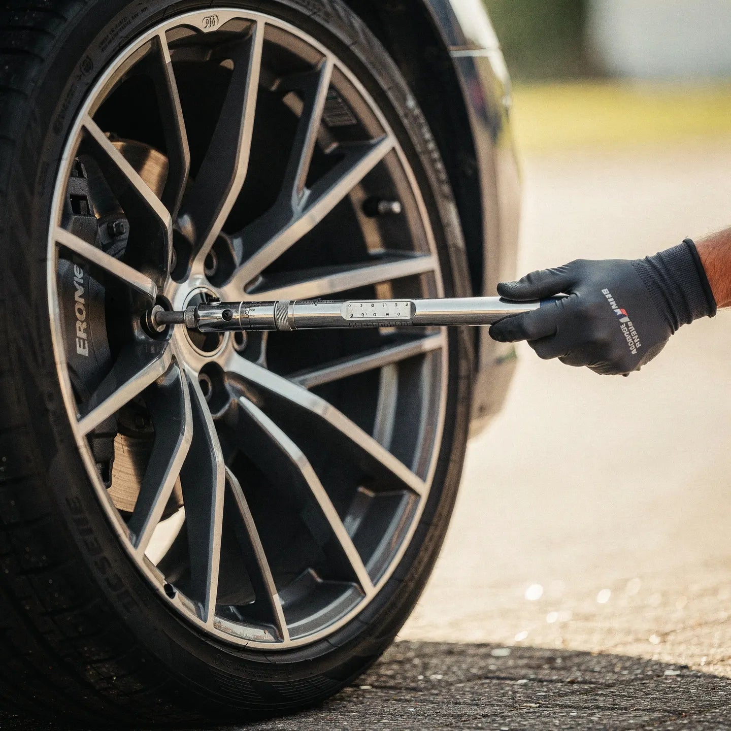Main gantée de technicien utilisant une clé dynamométrique calibrée pour serrer les écrous d'une jante design multi-branches, garantissant un couple de serrage conforme aux normes constructeur